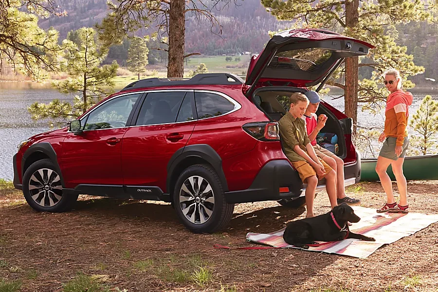 Family sitting on the tailgate of a Subaru Outback with their dog